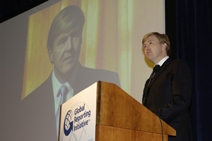 A speaker at a lectern with a projected portrait behind him